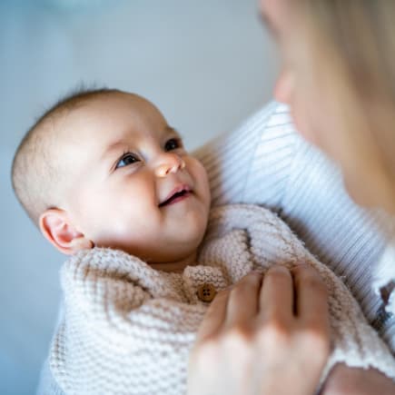 Eine Mutter hat ihr Baby auf dem Arm und es lächelt.