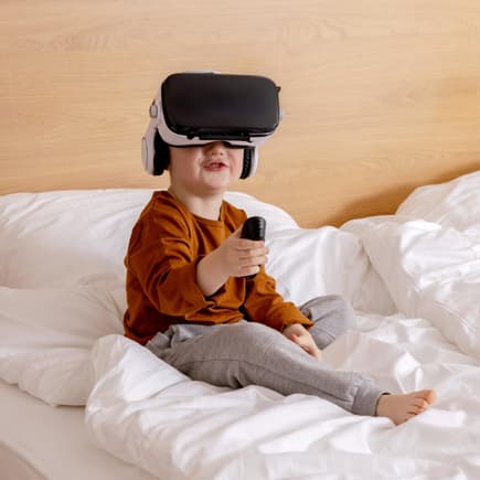 Ein kleiner Junge sitzt auf dem Bett und hat eine VR-Brille auf.