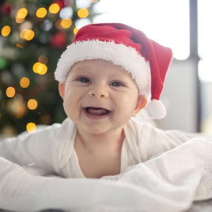 Ein Baby hat eine Weihnachtsmütze auf und lacht.