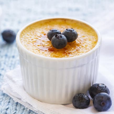 Eine Crème brulée steht auf dem Tisch und ist mit Blaubeeren garniert.