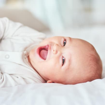 Ein kleines Baby liegt lachend auf dem Bett.