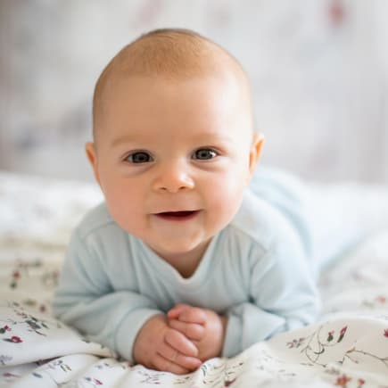 Ein Baby liegt auf dem Bauch und lächelt.