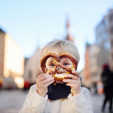 Ein kleiner Junge hält sich eine Brezel vor das Gesicht.