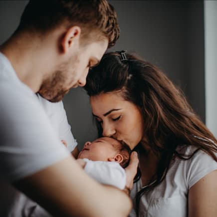 Junge Eltern küssen ihr frischgeborenes Baby. 
