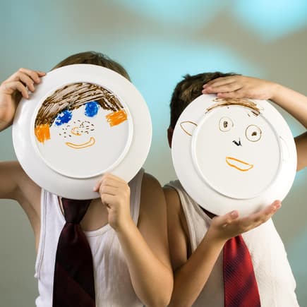 Zwei Jungen halten Teller hoch, auf die ein Gesicht gemalt ist.