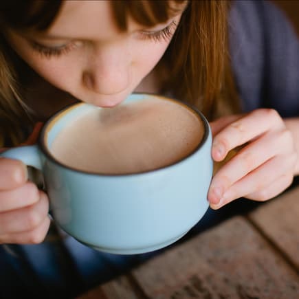 Mädchen schlürft heißen Kakao aus einer Tasse.
