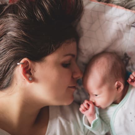 Junge Mama kuschelt mit ihrem Neugeborenen im Geburtshaus.