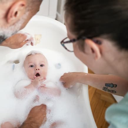 Eltern baden ihr Baby in einer Babybadewanne mit viel Badezusatz und Schaum.
