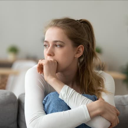 Junge Frau sitzt traurig und nachdenklich zu Hause