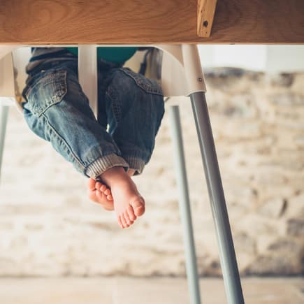 Kinderbeine unterm Tisch im Hochstuhl