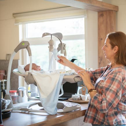 Mama legt Baby in elektrische Babyschaukel