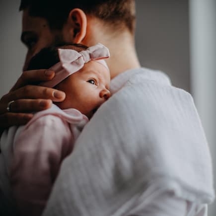 Papa hält neugeborene Tochter im Arm