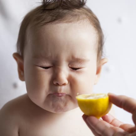 Ein kleines Baby isst eine Zitrone und verzieht das Gesicht.