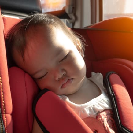 Ein Baby sitzt im Kindersitz des Autos, während die Sonne hereinscheint.