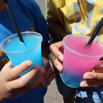 Zwei Kinder trinken rosa-blauen Slush. 