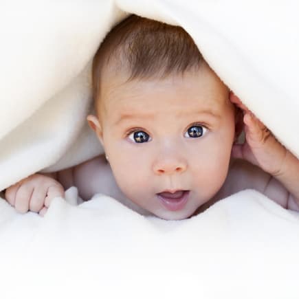 Baby guckt unter weißer Decke hervor.