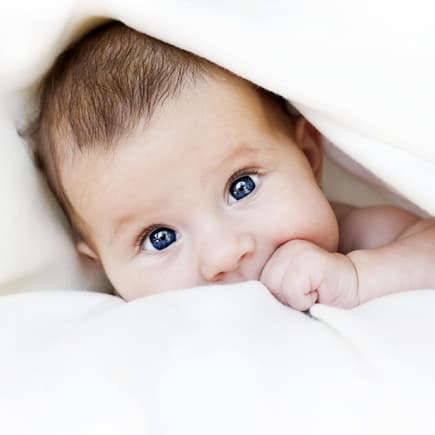 Baby guckt unter Decke hervor.