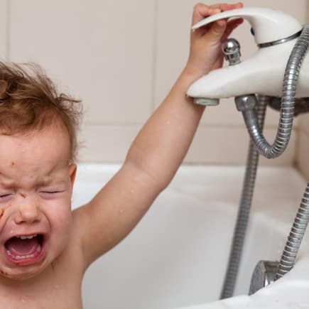 Ein Baby schreit beim Baden in der Badewanne und kneift dabei die Augen zu.