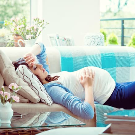 Schwangere Frau liegt auf dem Sofa und ruht sich aus – sie hat starke Schwangerschaftsbeschwerden.