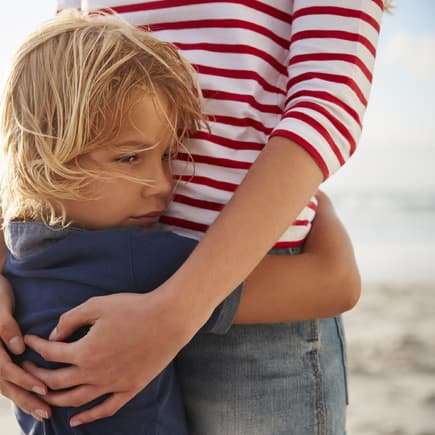 Mutter umarmt Sohn am Strand.