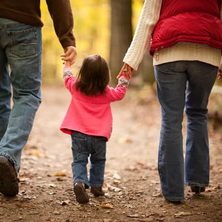 Kleines Mädchen übt mit seinen Eltern das Laufen