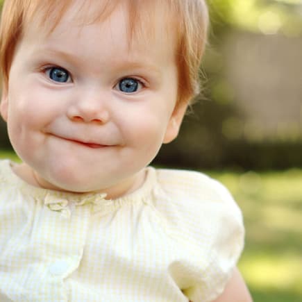 Ein Baby-Mädchen mit roten Haaren lächelt und freut sich über ihren englischen Mädchennamen.