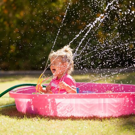 Kleines Mädchen spielt in einem Plantschbecken mit einem Wasserspielzeug.