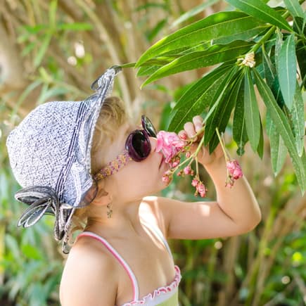 Mädchen mit Hut und Sonnenbrille riecht an einem Blumenstrauch im Garten