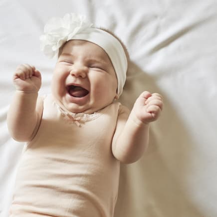 Ein Baby-Mädchen lacht niedlich und kneift dabei die Augen zu. 