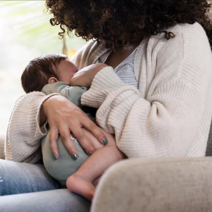 Eine Frau stillt ihr Baby sitzend auf dem Sessel.