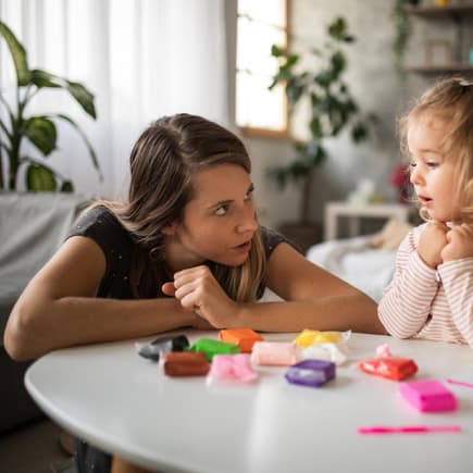 Mutter spricht mit ihrer kleinen Tochter am Spieltisch.