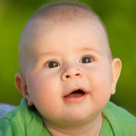 Baby-Junge grinst aufgeweckt nach vorne.