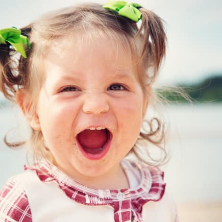 Kleines niedliches Baby-Mädchen lacht am Strand und freut sich über ihren starken Namen.