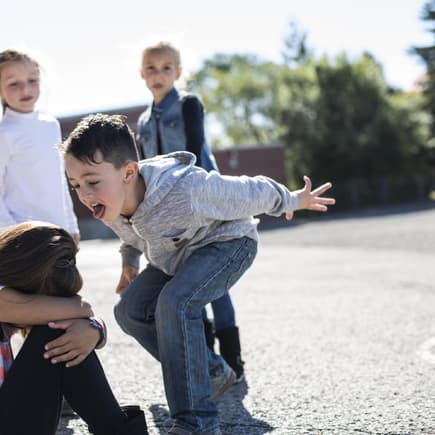 Mobbing an der Grundschule: Kinder ärgern ein kleines Mädchen auf dem Schulhof.