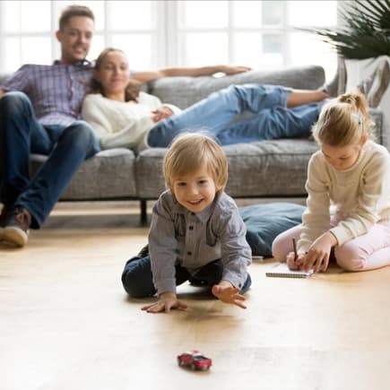 Kinder spielen, Eltern sitzen entspannt auf dem Sofa.