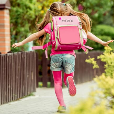 Mädchen mit einem bestickten Schulranzen läuft den Gehweg entlang.