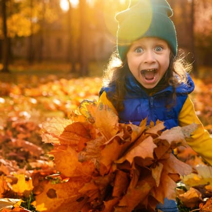 Lachendes Mädchen spielt im Herbstlaub.