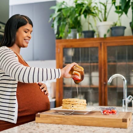 Schwangere Frau gibt etwas Agavendicksaft auf ihre Pfannkuchen.