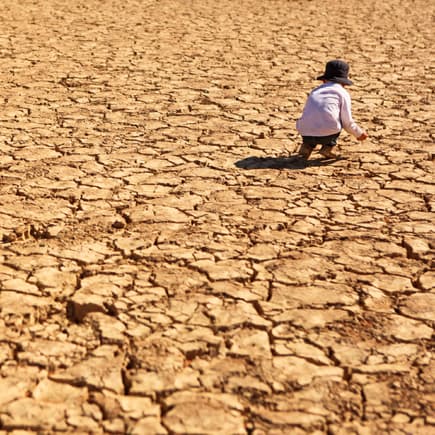 Folgen des Klimawandels: Ein kleines Kind spielt auf einem ausgetrocknetem Feld. 