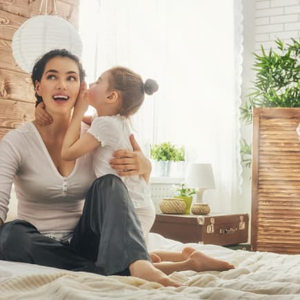 Mädchen flüstert seiner Mama etwas ins Ohr.