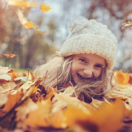 Mädchen mit Mütze im Herbstlaub.