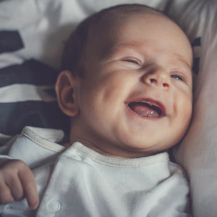 Kleiner Baby-Junge lacht zufrieden und liegt auf dem Bett. 