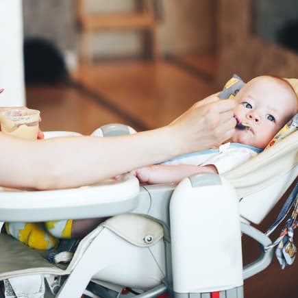 Baby liegt und isst im Hochstuhl