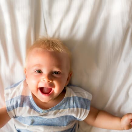 Baby-Junge liegt auf dem Bett und lacht.