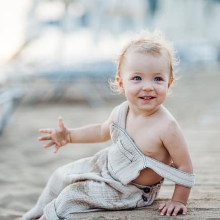 Ein kleines Mädchen sitzt mit Sand an den Händen am Strand.