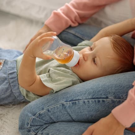 Ein kleiner Baby-Junge trinkt liegend Fencheltee aus einer Nuckelflasche. 