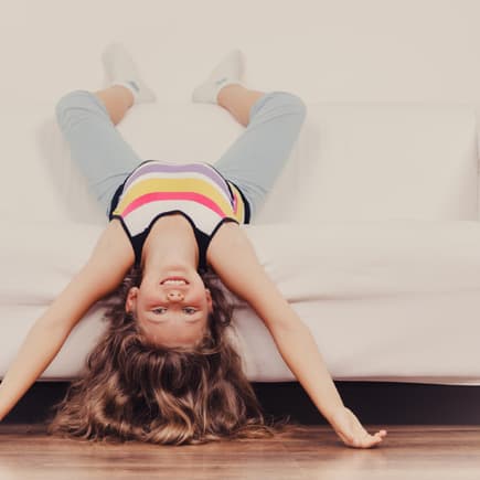 Kleines Mädchen Kind mit langen Haaren kopfüber auf dem Sofa.