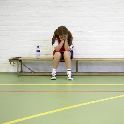 Ein Mädchen sitzt beim Schulsport frustriert auf der Bank. 