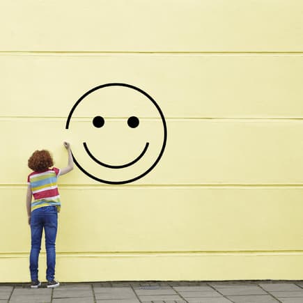 Mädchen malt Smiley an gelbe Wand.