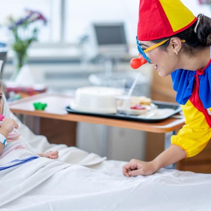 Ein weiblicher Klinik-Clown überrascht ein kleines Mädchen im Krankenhaus.